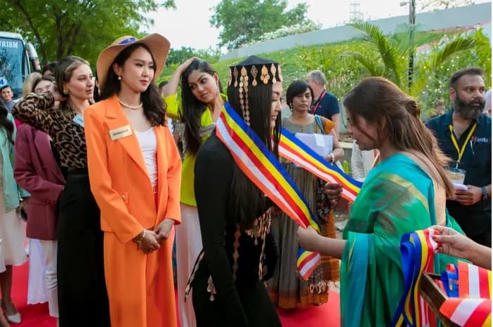 Women in sashes and colourful outfits standing outdoors among a crowd