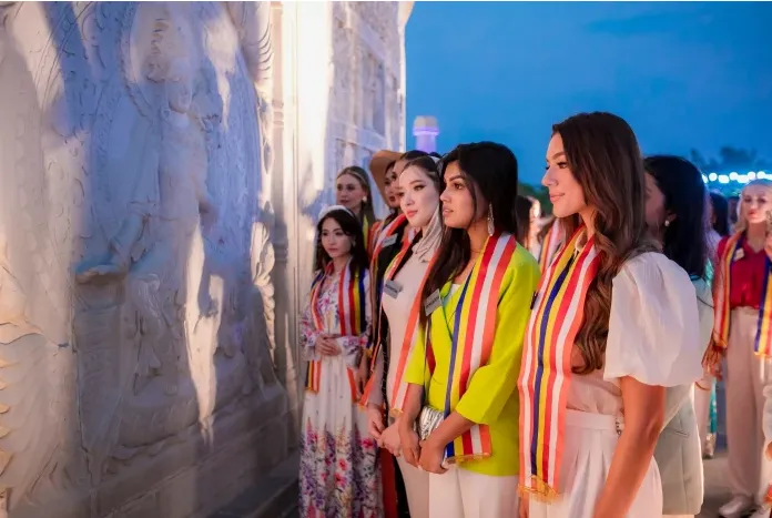 Row of women in sashes standing beside a carved stone wall