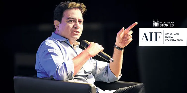 Man speaking into a microphone and gesturing while seated on a stage