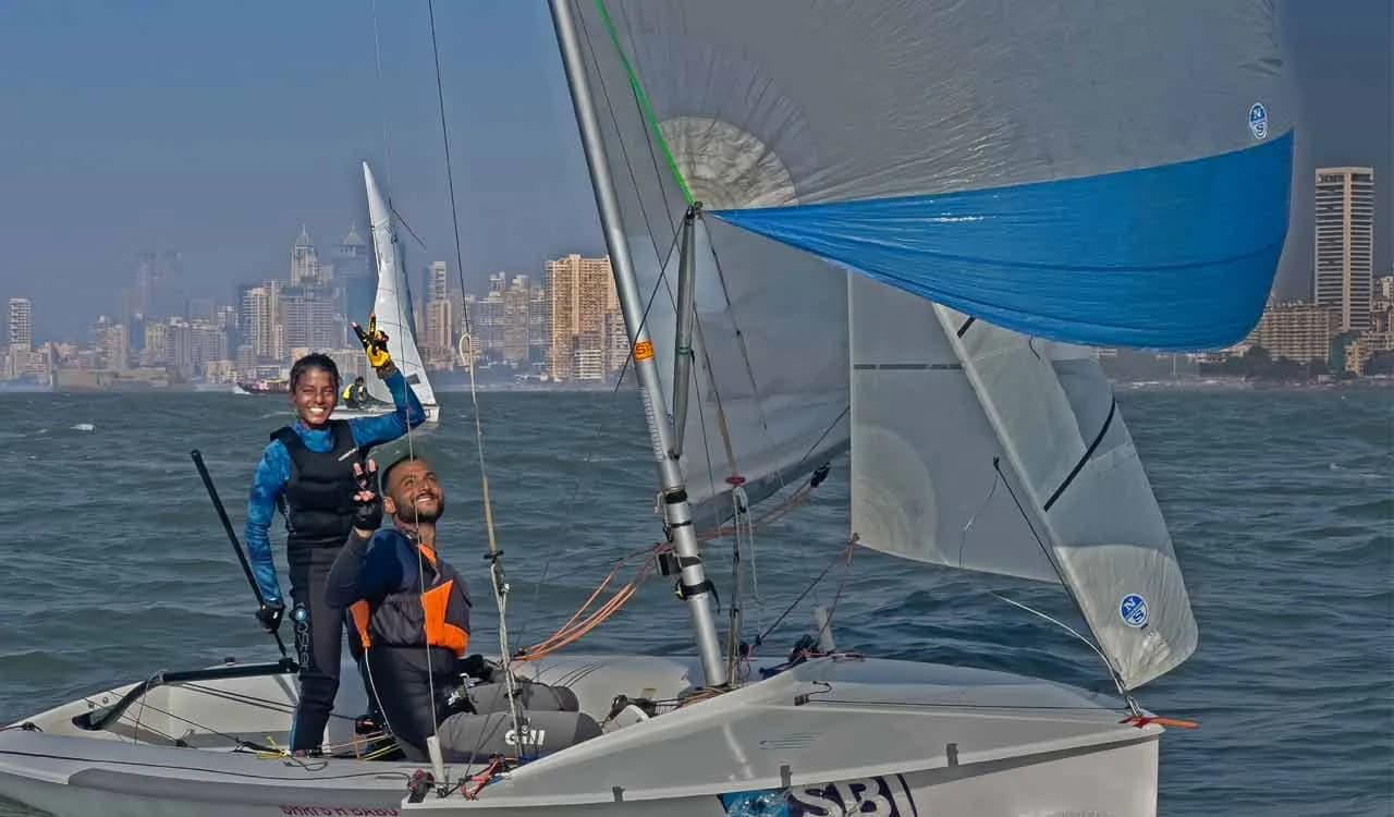 Two people on a small sailing boat with a city skyline behind
