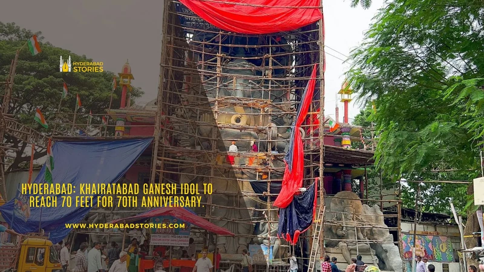 News graphic of a tall idol under construction on scaffolding draped in red cloth