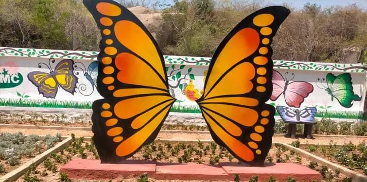 Large orange butterfly sculpture beside a painted wall in a garden
