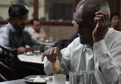 Men seated at a cafe table, one dipping bread into a cup