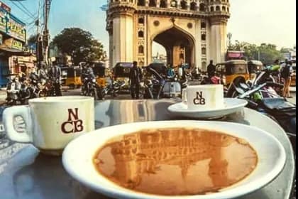 Two cups of coffee on a table with a monument and street traffic behind