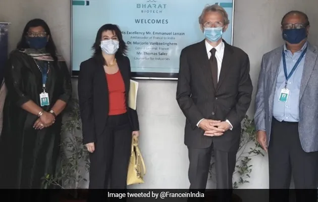 Four people in masks standing before a welcome sign indoors