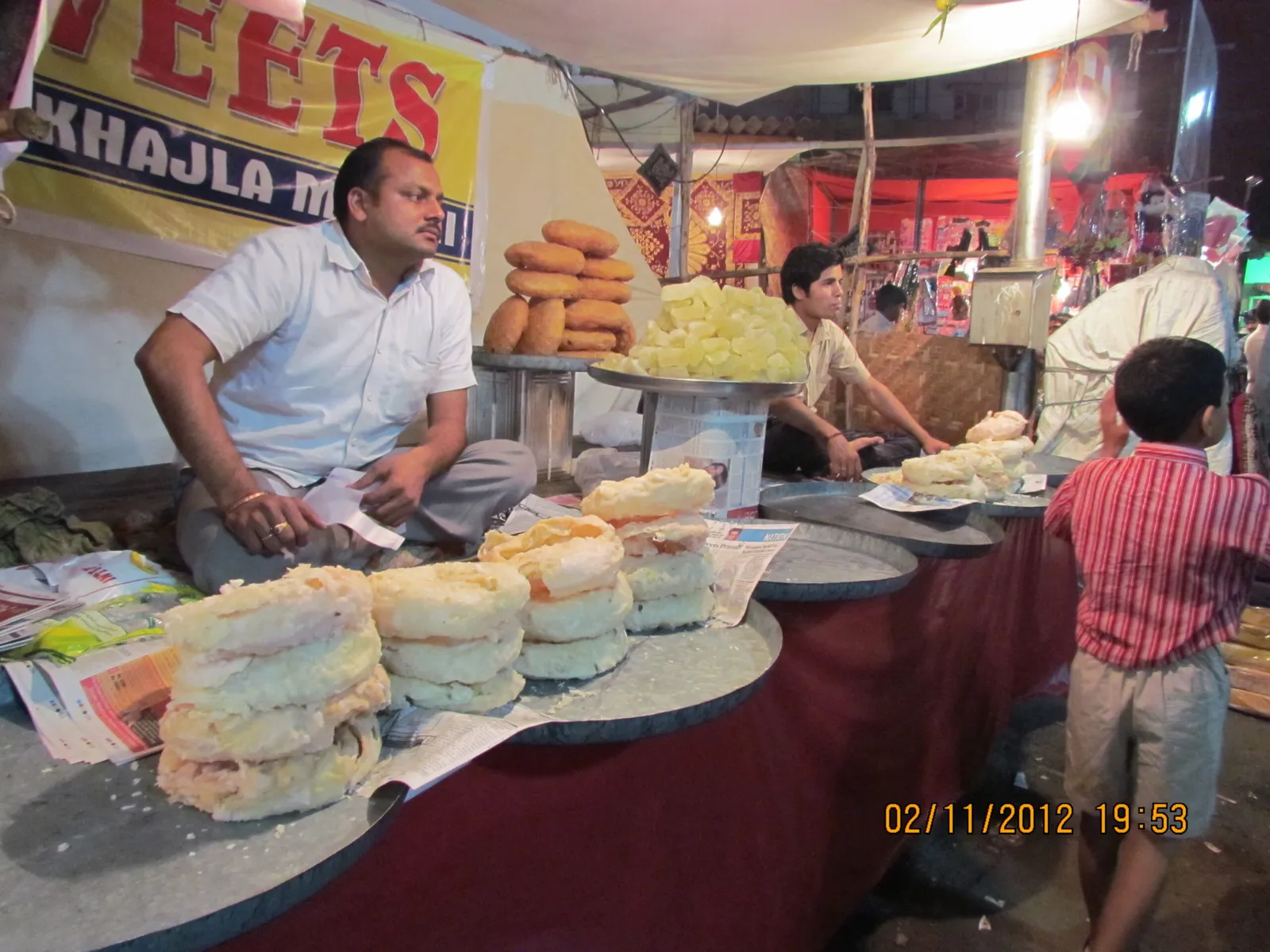 Vendors preparing sweets at a lit street stall with a child watching