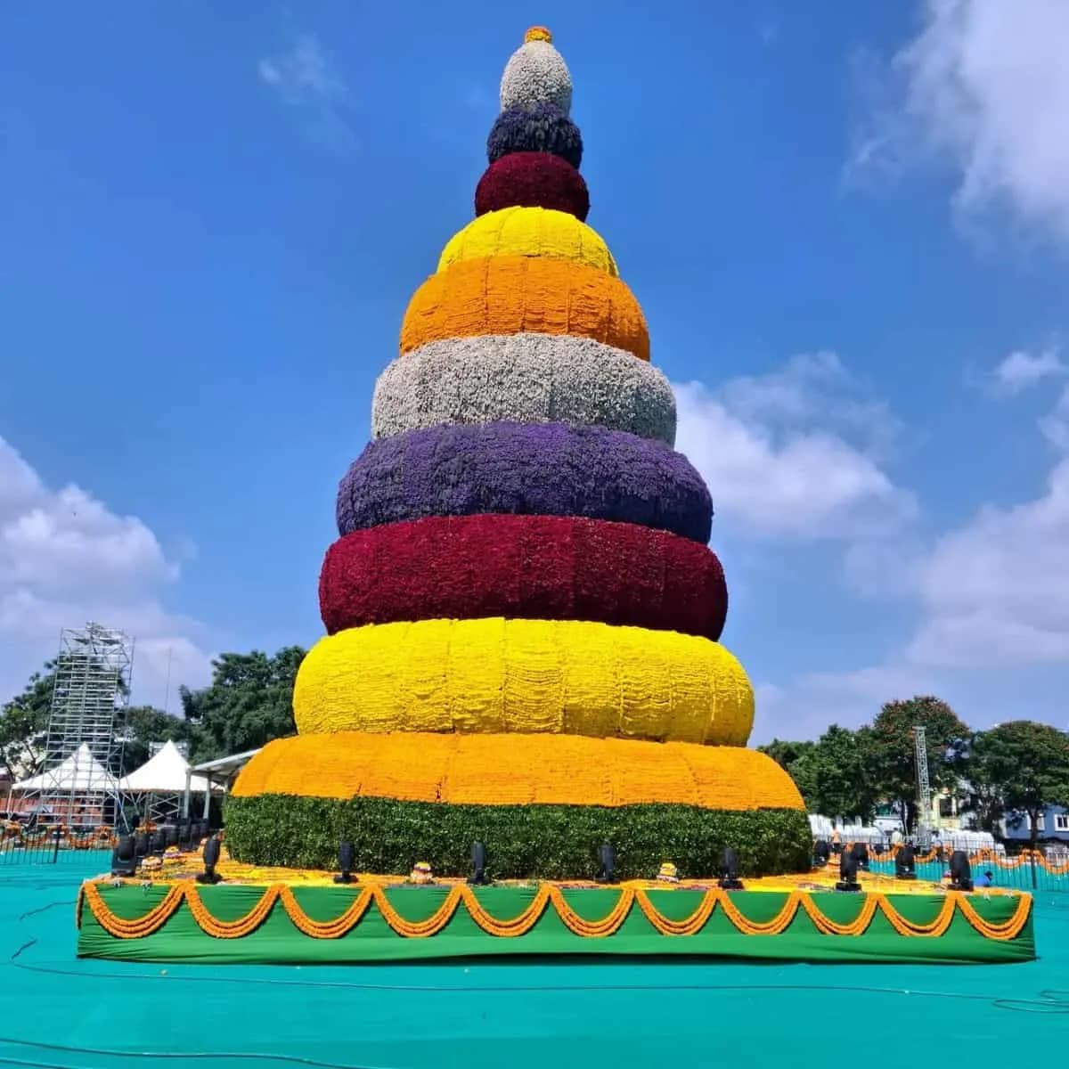 Tall tiered floral arrangement in bright colours beside a temple
