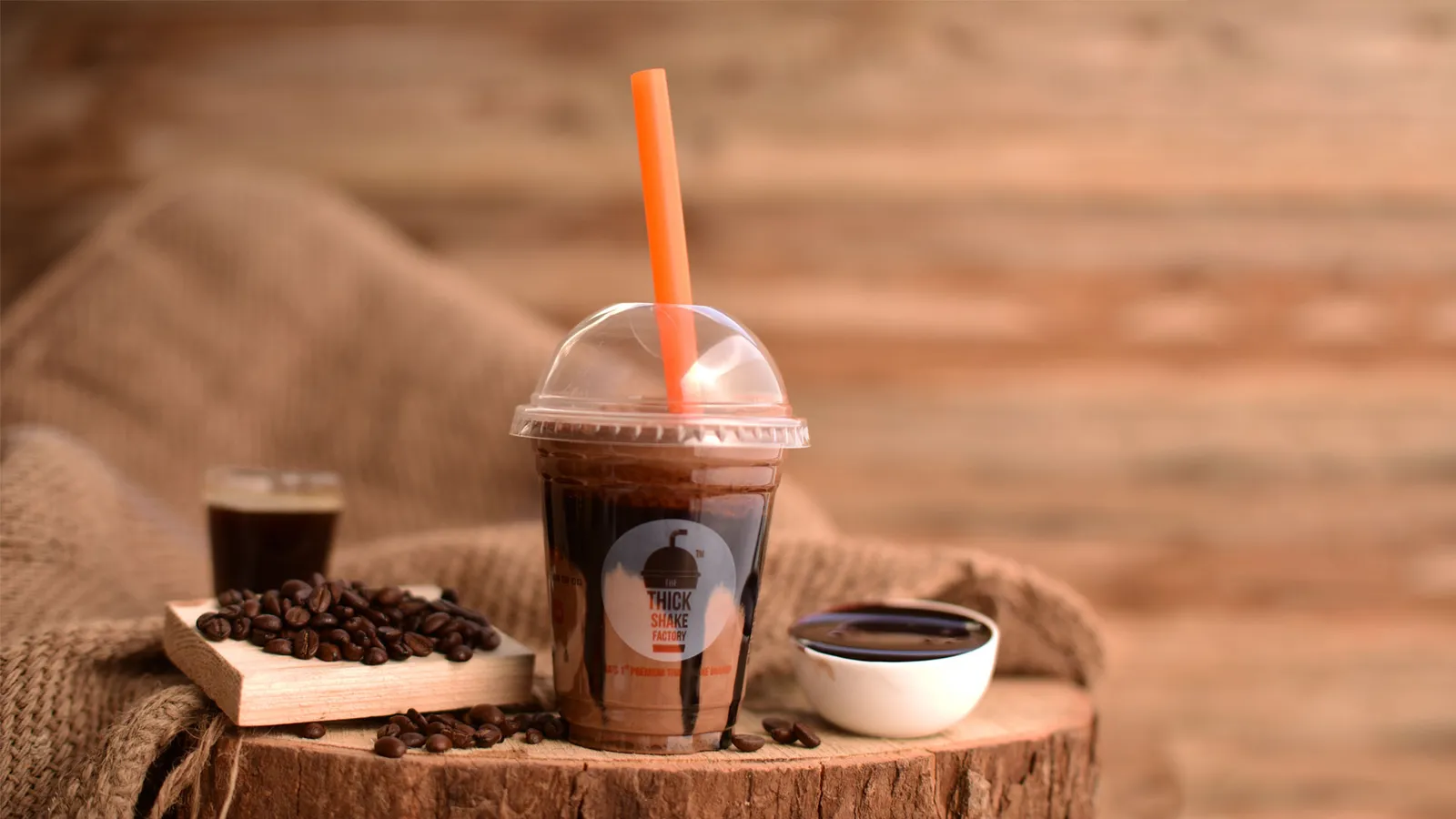 Iced coffee in a plastic cup on a wooden slice beside scattered coffee beans
